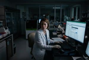 Woman at computer in a dark lab looking suspicious.